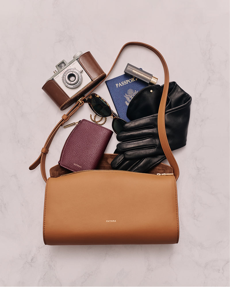 Handbag with gloves, wallet, passport, sunglasses, camera, and lipstick on marble surface