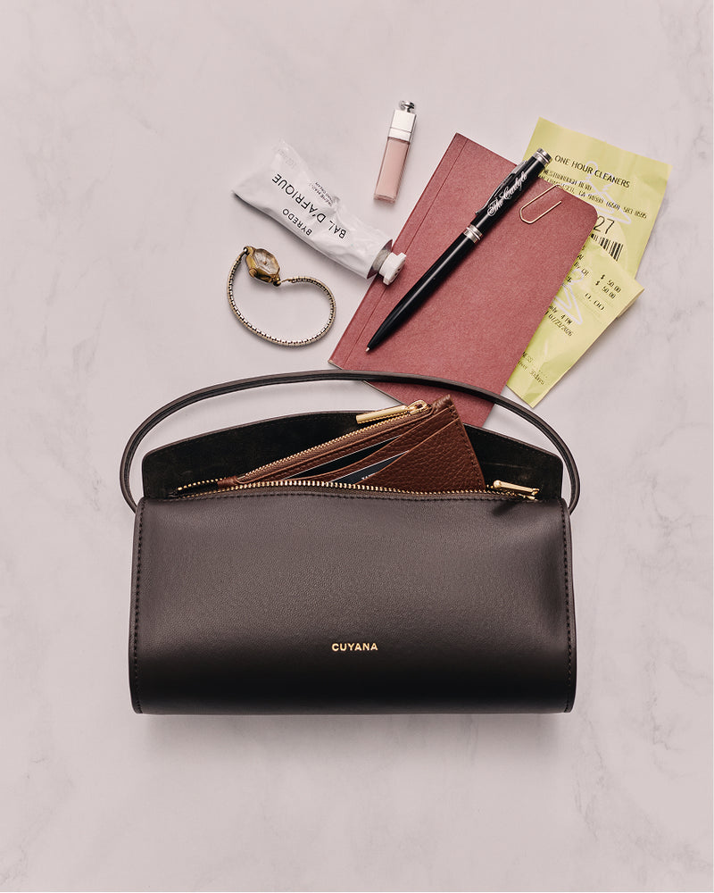 Handbag with zipper, notebooks, pen, bracelet, lip balm, and tickets on surface