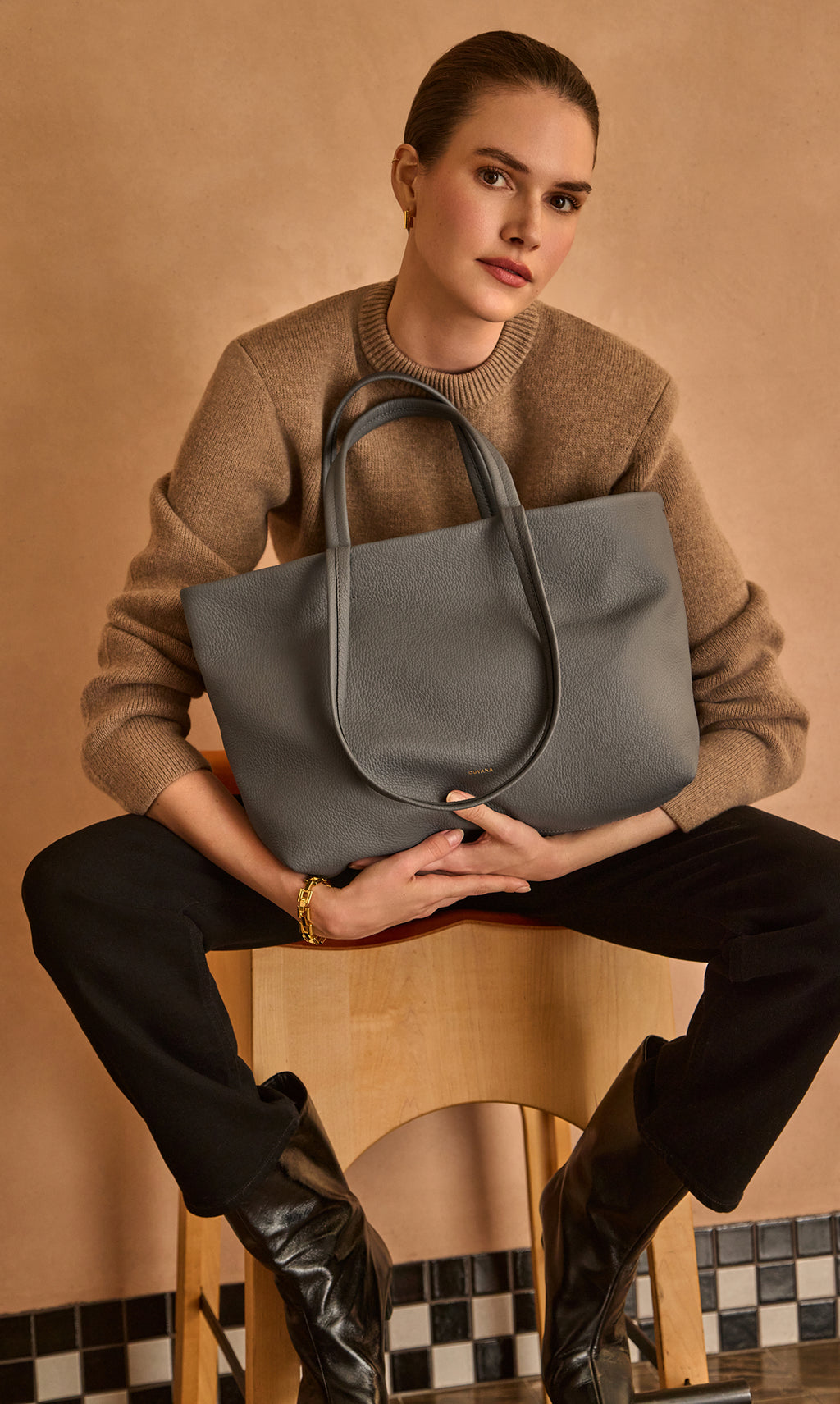 Person sitting with tote bag on lap, wearing sweater and boots.
