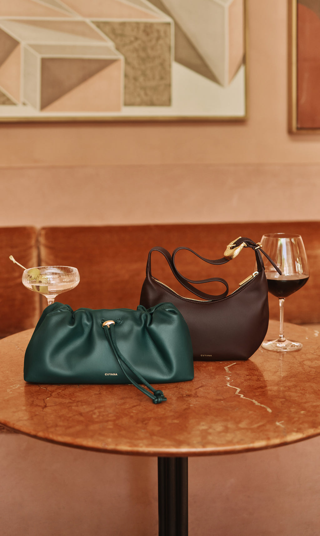 Two handbags on a table with a cocktail and a wine glass.