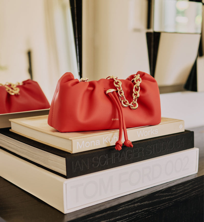 Red handbag with chain on stacked books in a room with a mirrored surface.