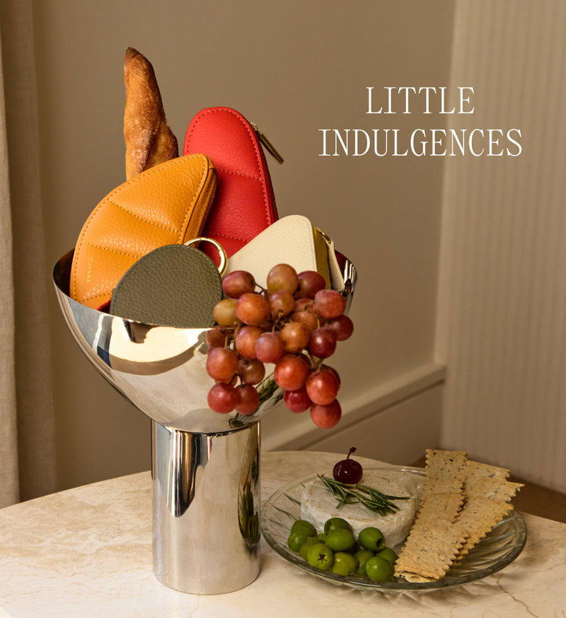 A silver vase holds small pouches with bread and grapes; crackers and olives on the table.