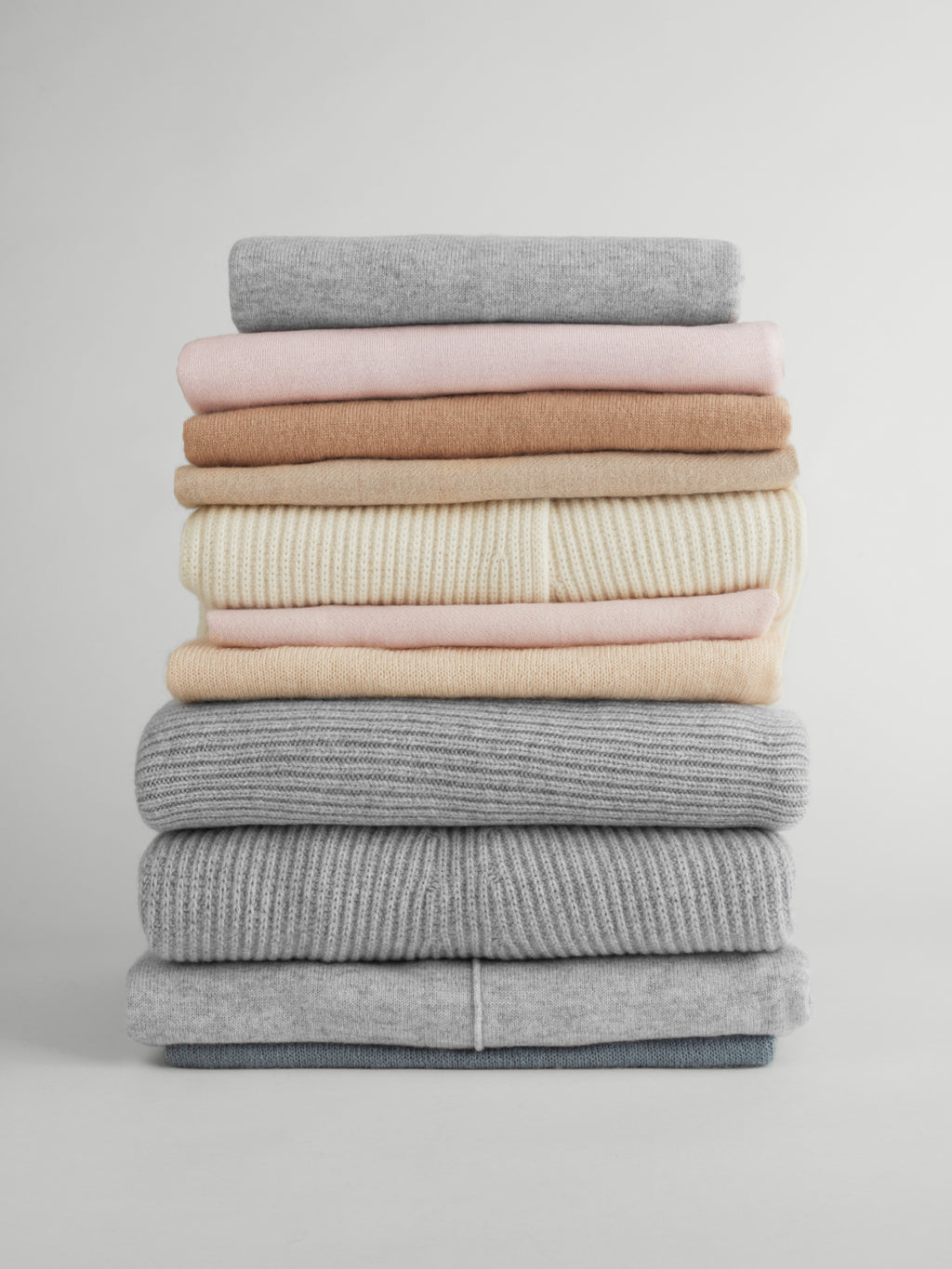 Stack of folded sweaters on a plain background.