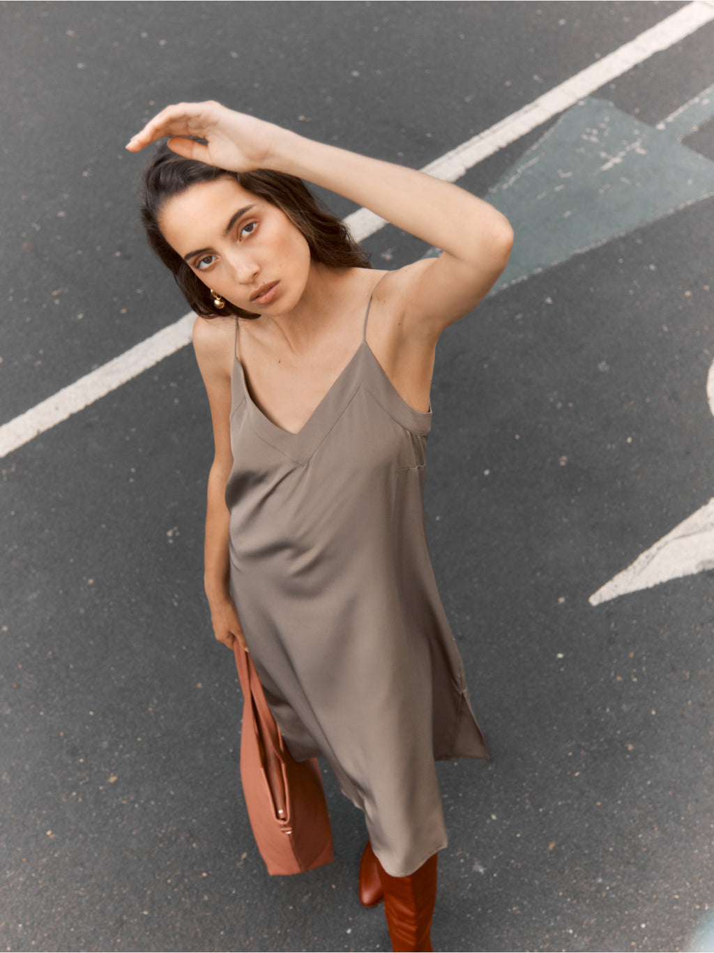 Woman standing on a street with one hand raised, holding a bag.