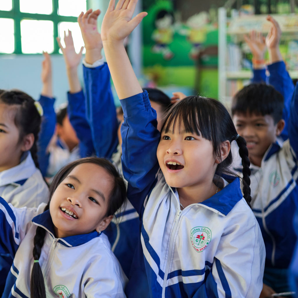 Children in uniforms raising their hands in a classroom.
