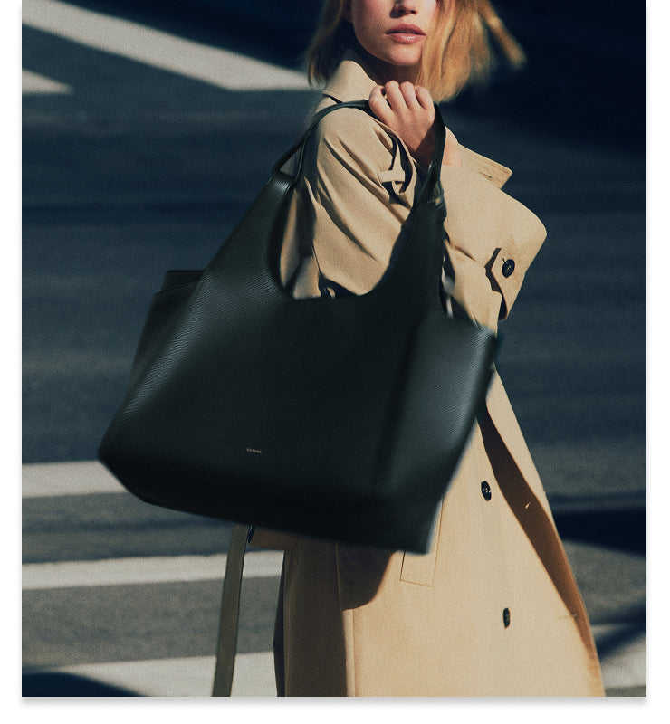 Person in coat holding large handbag outdoors.