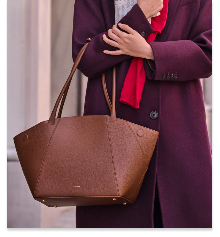 Person holding bag, wrapped in cape, standing by a wall.
