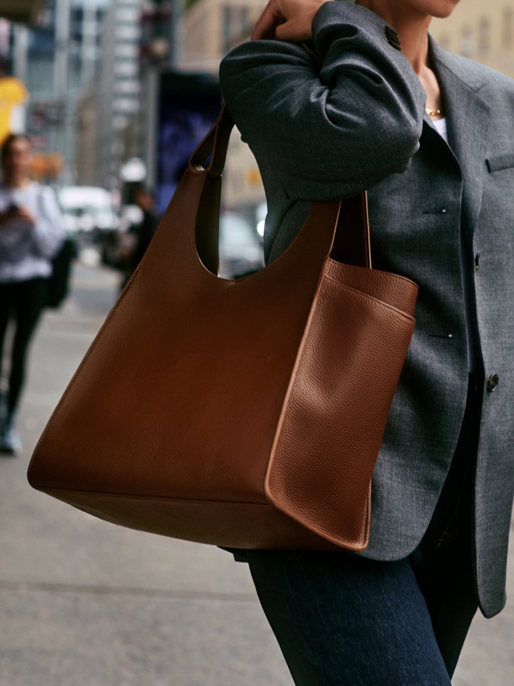 Person carrying large handbag on city sidewalk.