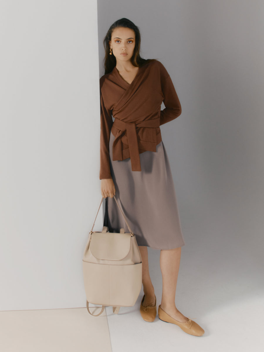 Woman standing holding a bag with one hand in a studio setting.