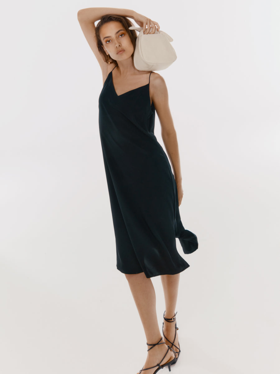 Woman in a dress posing with a bag on her shoulder and one hand on her head.