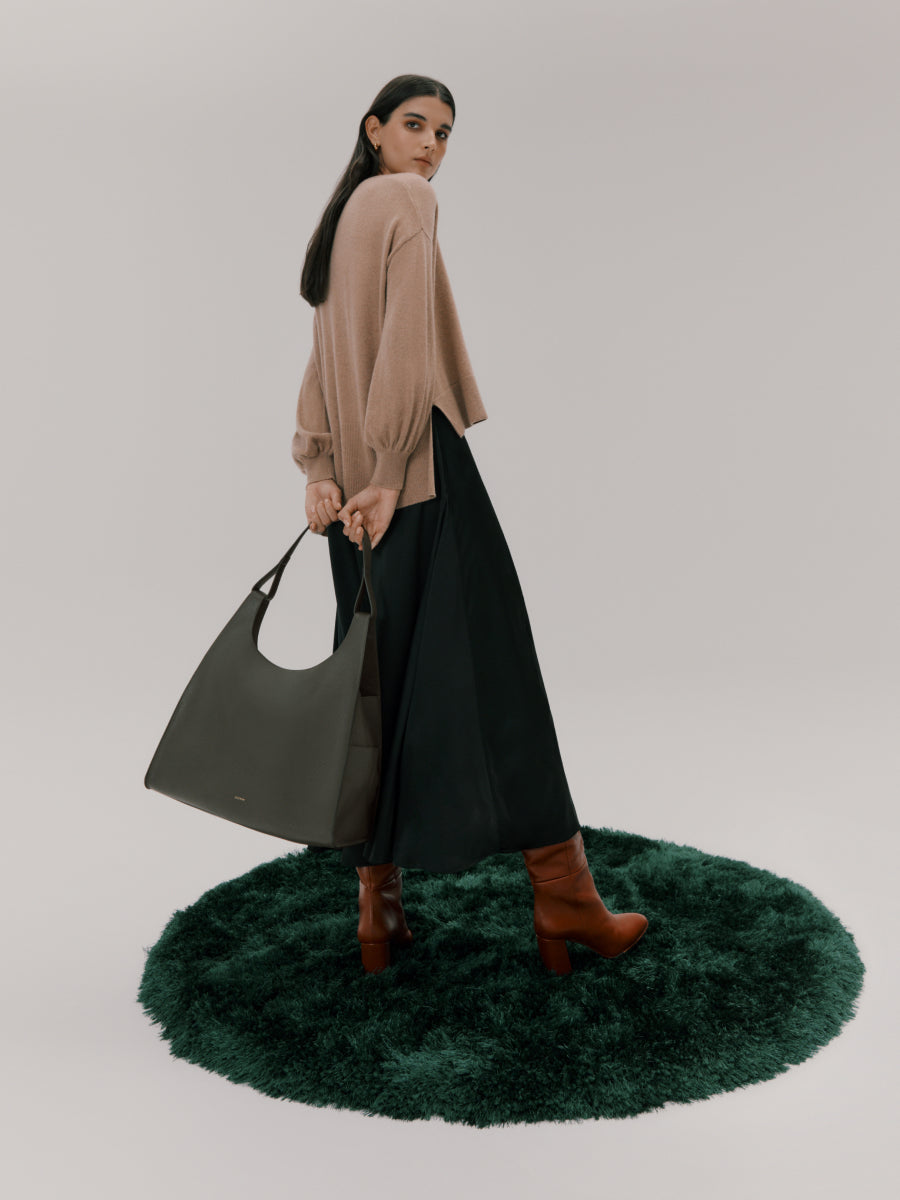 Woman standing on a round rug, holding a bag and looking over her shoulder.