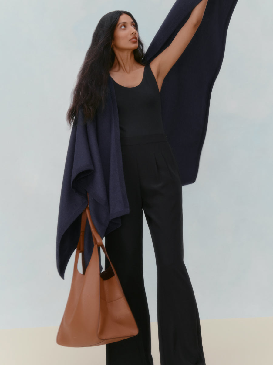 Woman holding a scarf above her head with a bag on her shoulder.