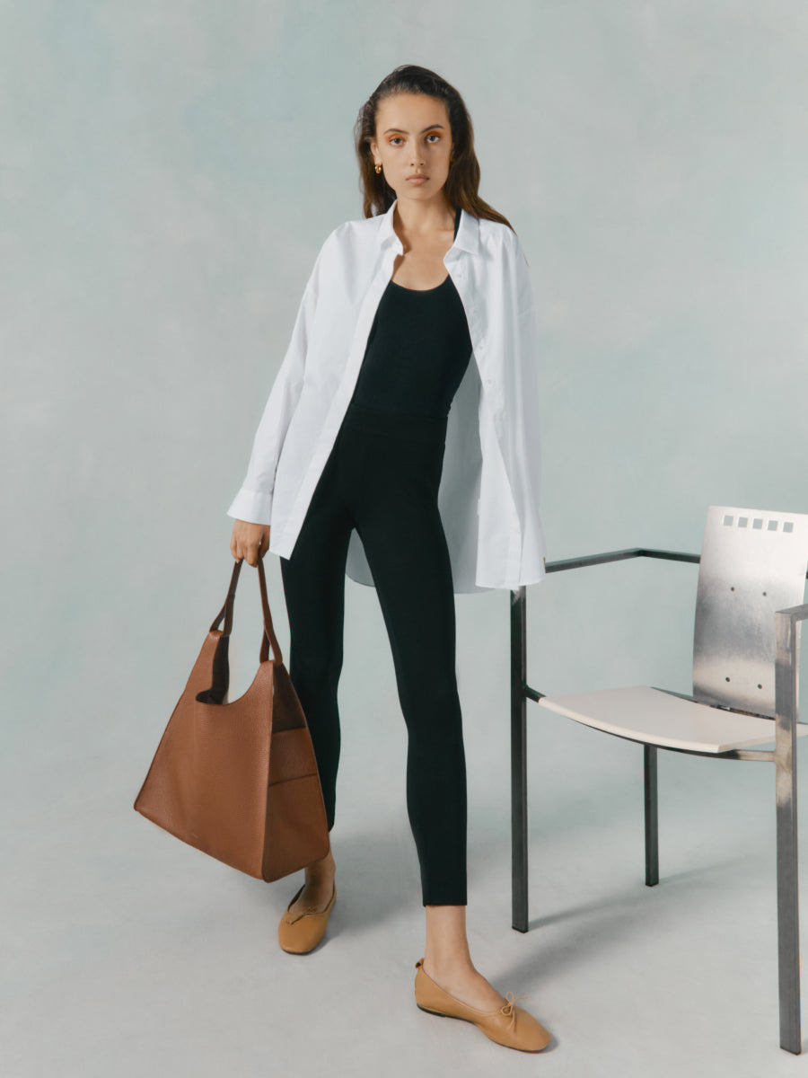 Woman standing next to a chair holding a bag.