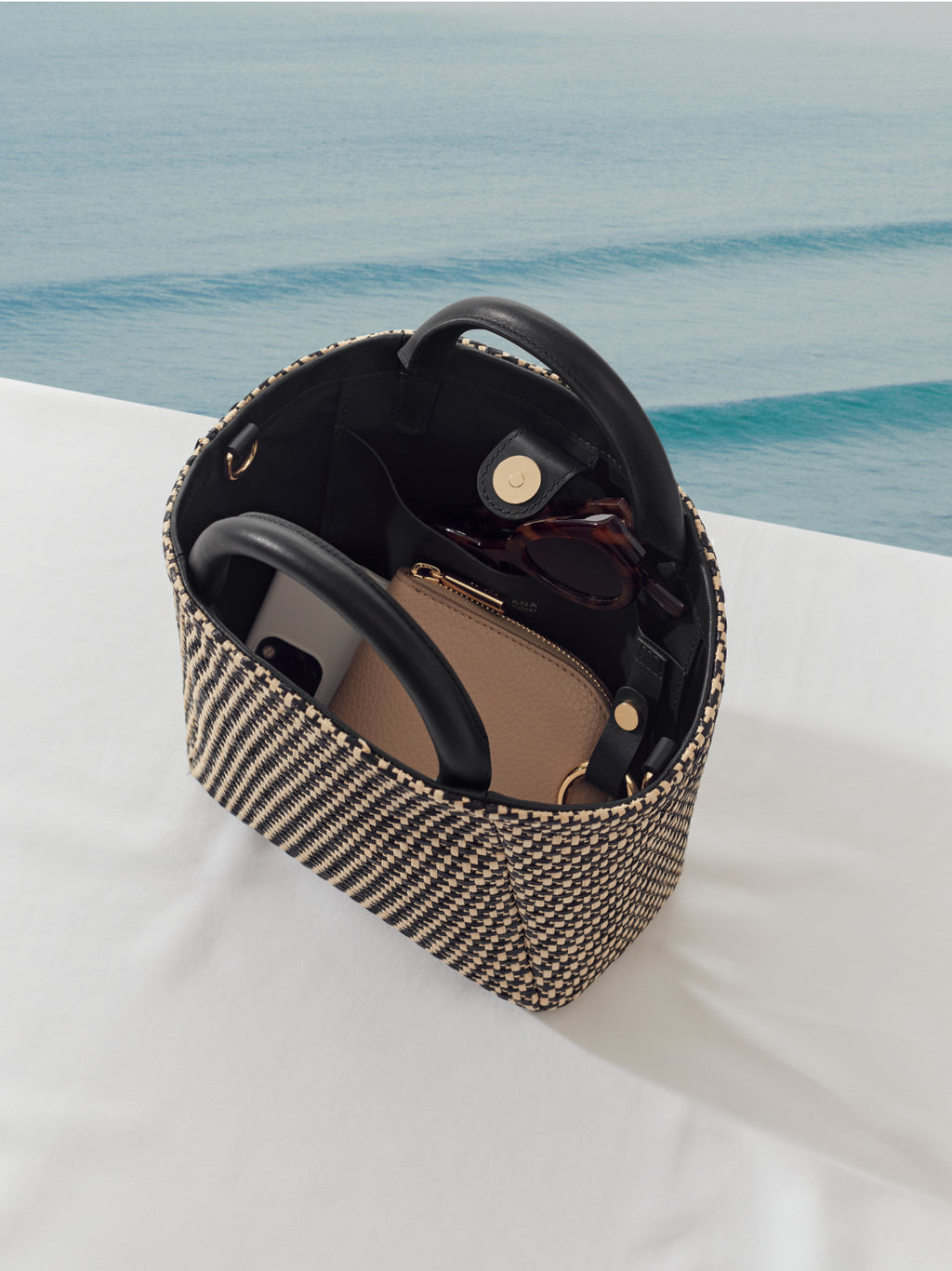 Open handbag with visible items including purse, glasses, and phone on a surface near the beach