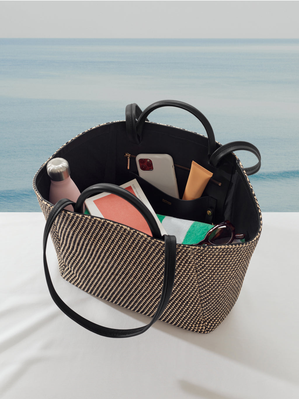 Open bag with handle on table containing water bottle, phone, notebook, and other items inside