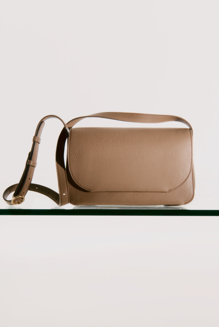 Shoulder bag with strap standing upright on glass surface.