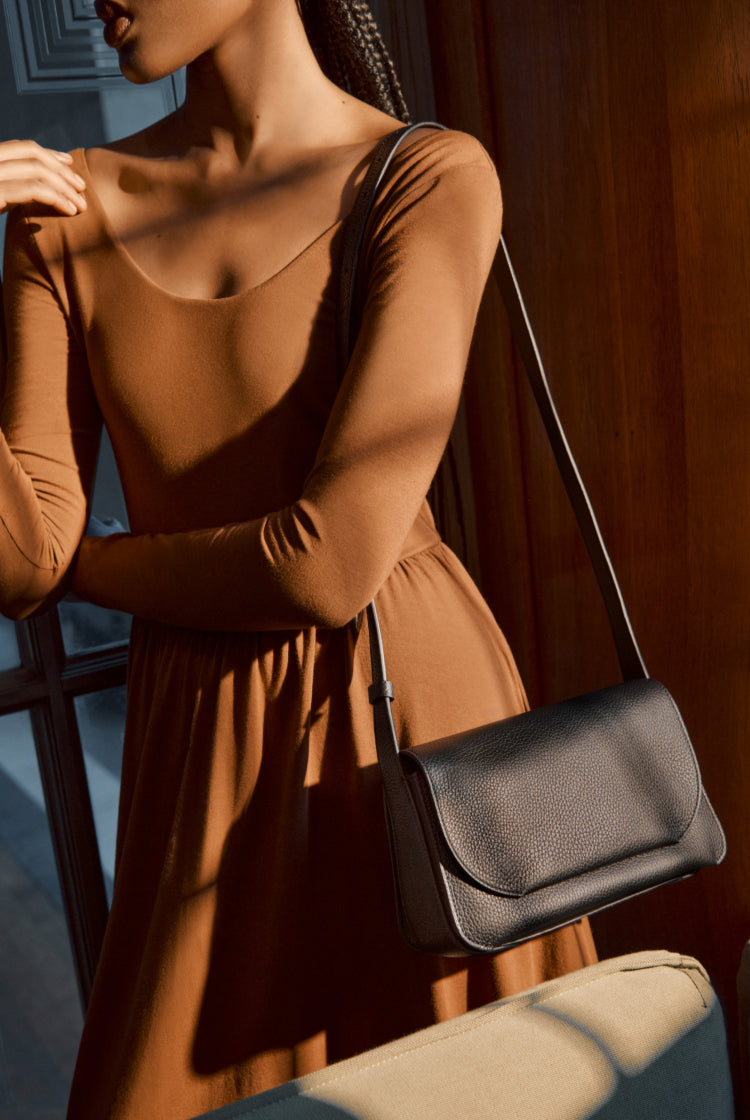 Woman in dress standing with a shoulder bag indoors.
