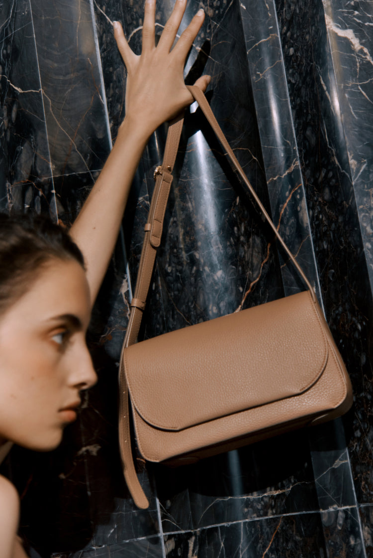 Person reaching for a handbag hanging on a marbled wall.