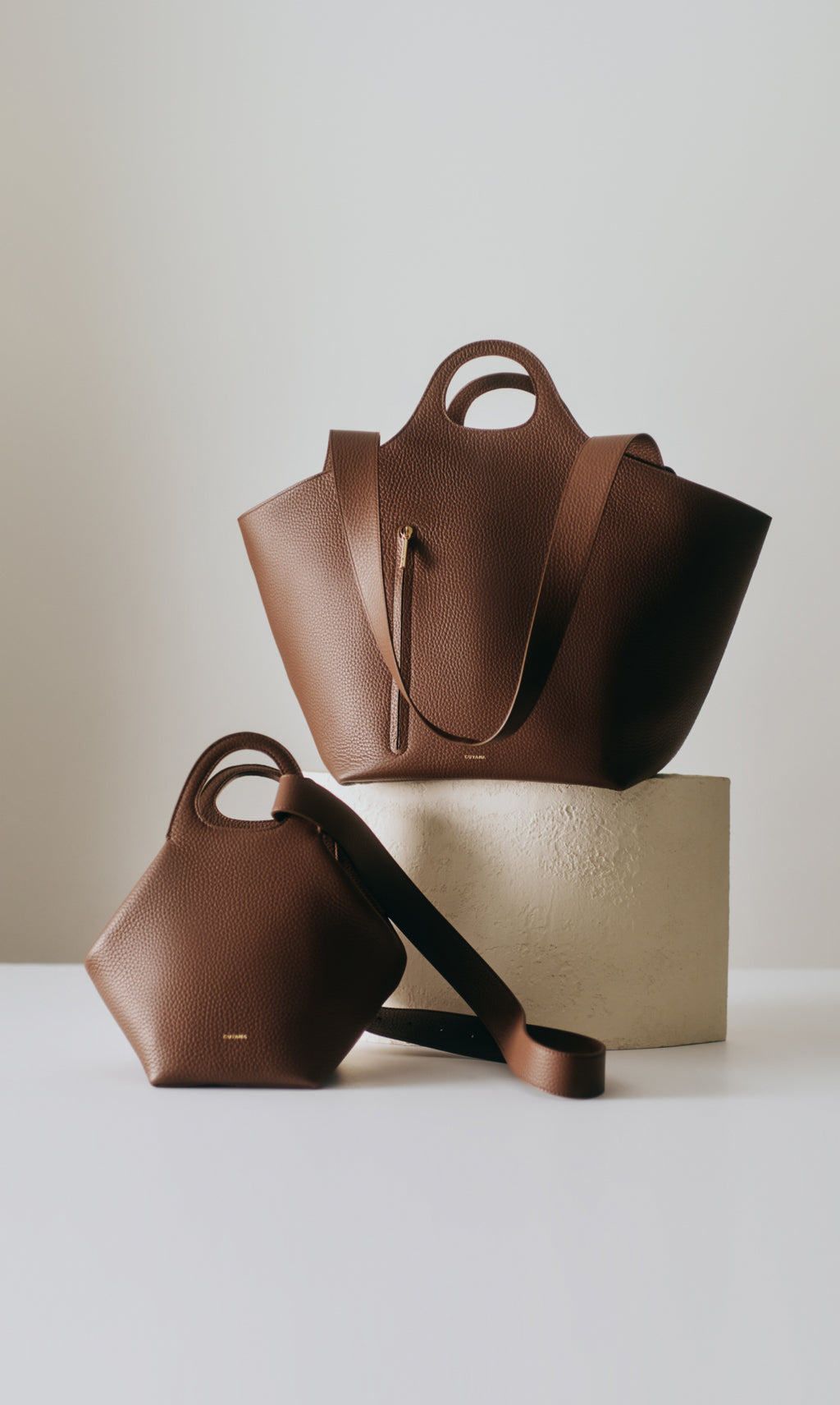 Two handbags with long straps displayed on white surfaces