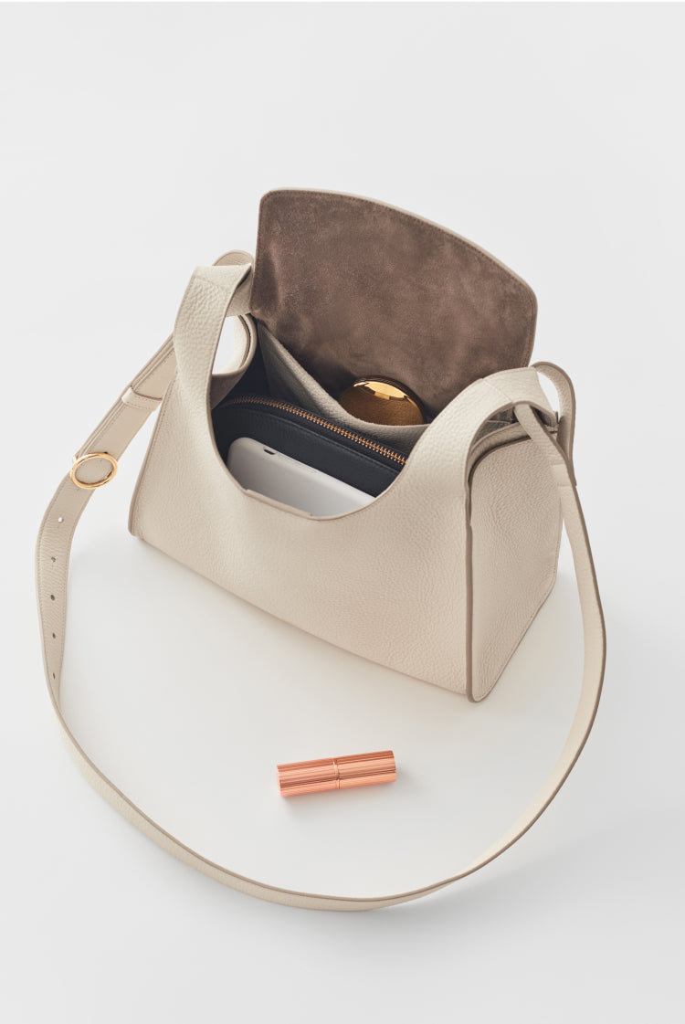 Handbag open with items inside and a lipstick beside it.