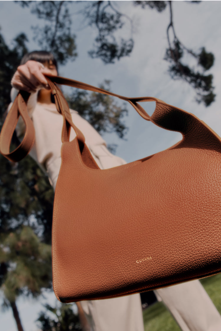 Person holding a handbag outdoors with trees in the background.