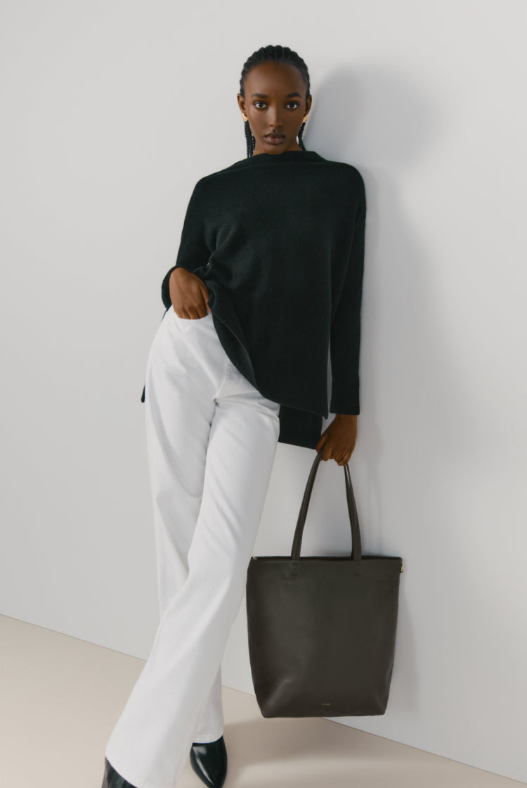 Woman standing with hand on hip holding a tote bag.