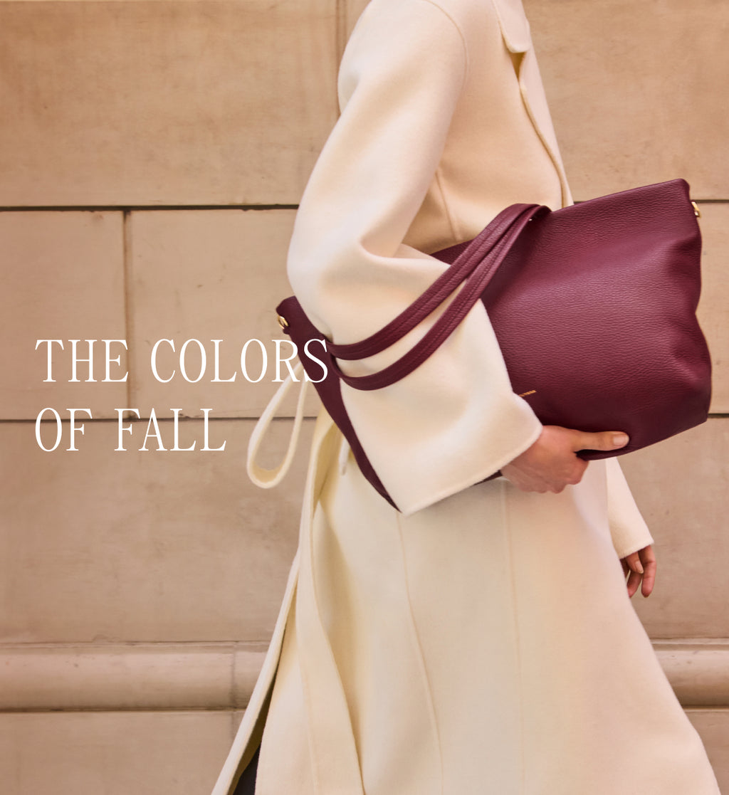 Person holding a large handbag while walking past a wall.