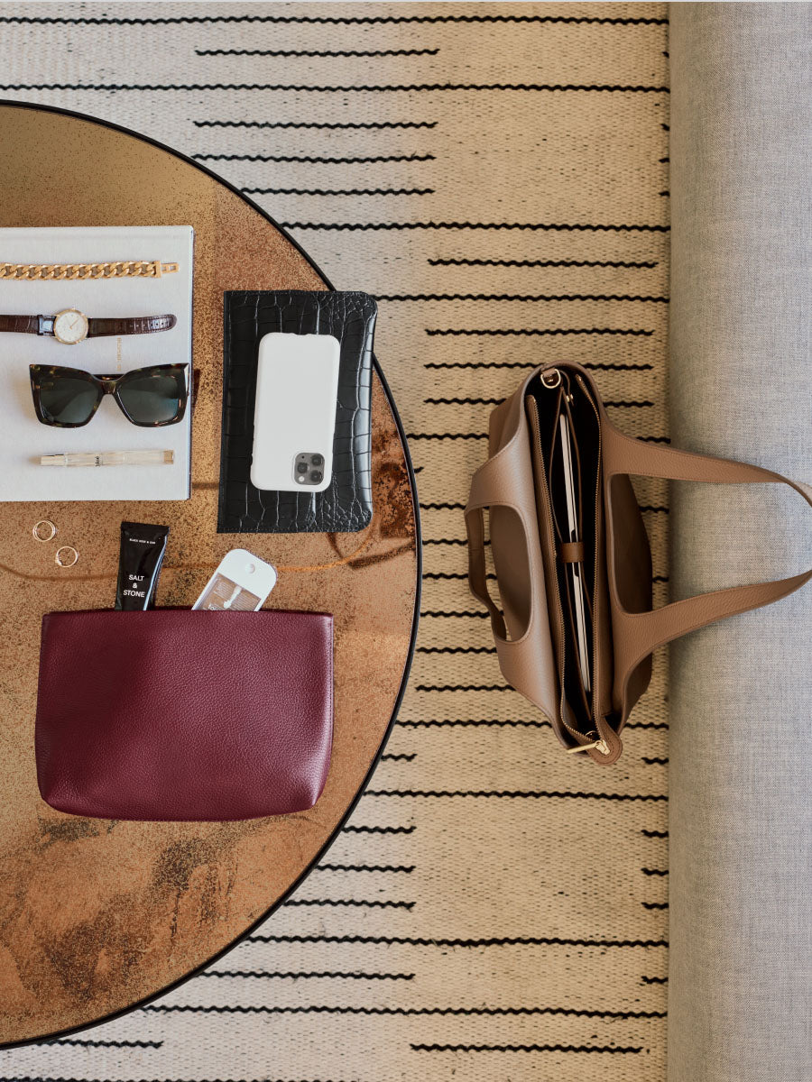 Items arranged on a table include a travel bag, croc-embossed leather phone case, and red pouch.