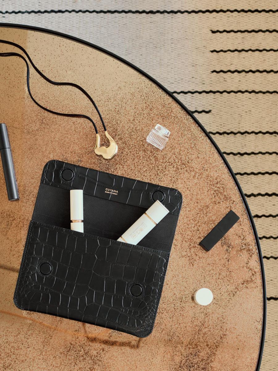 Table with croc-embossed leather clutch, lipsticks, necklace, and small grooming items.
