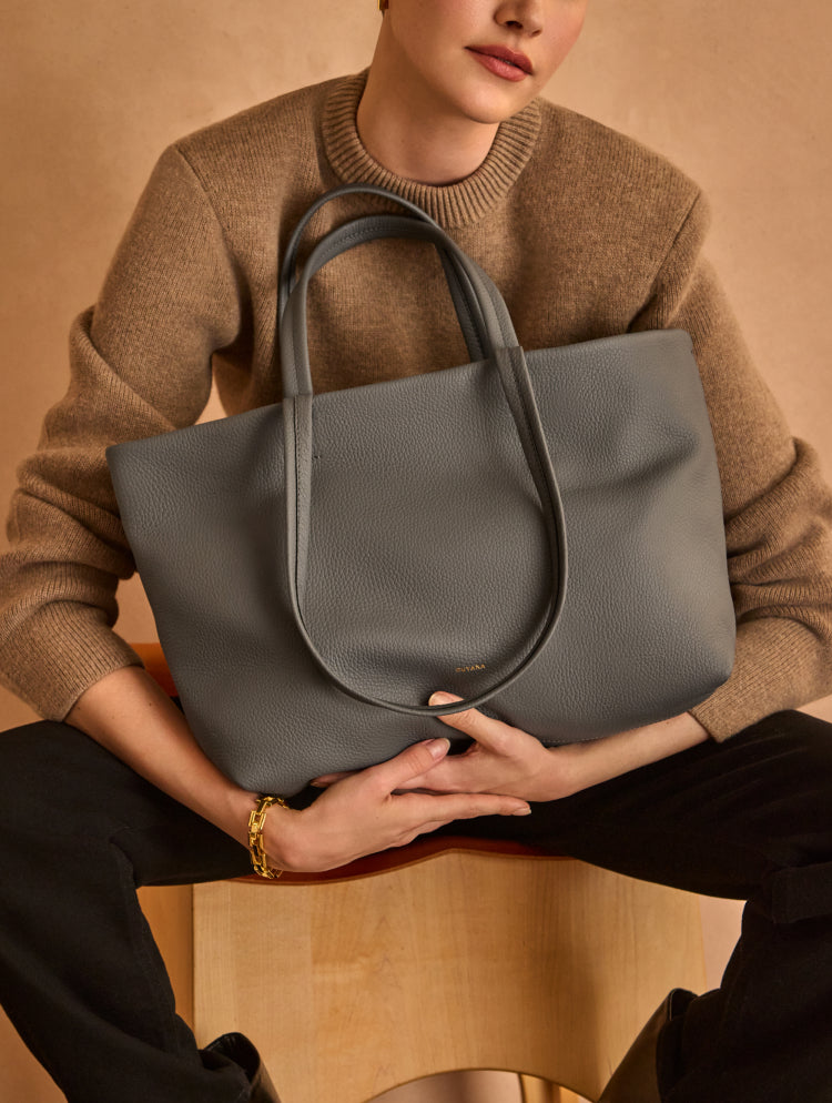 Person holding a large tote bag while sitting on a chair.