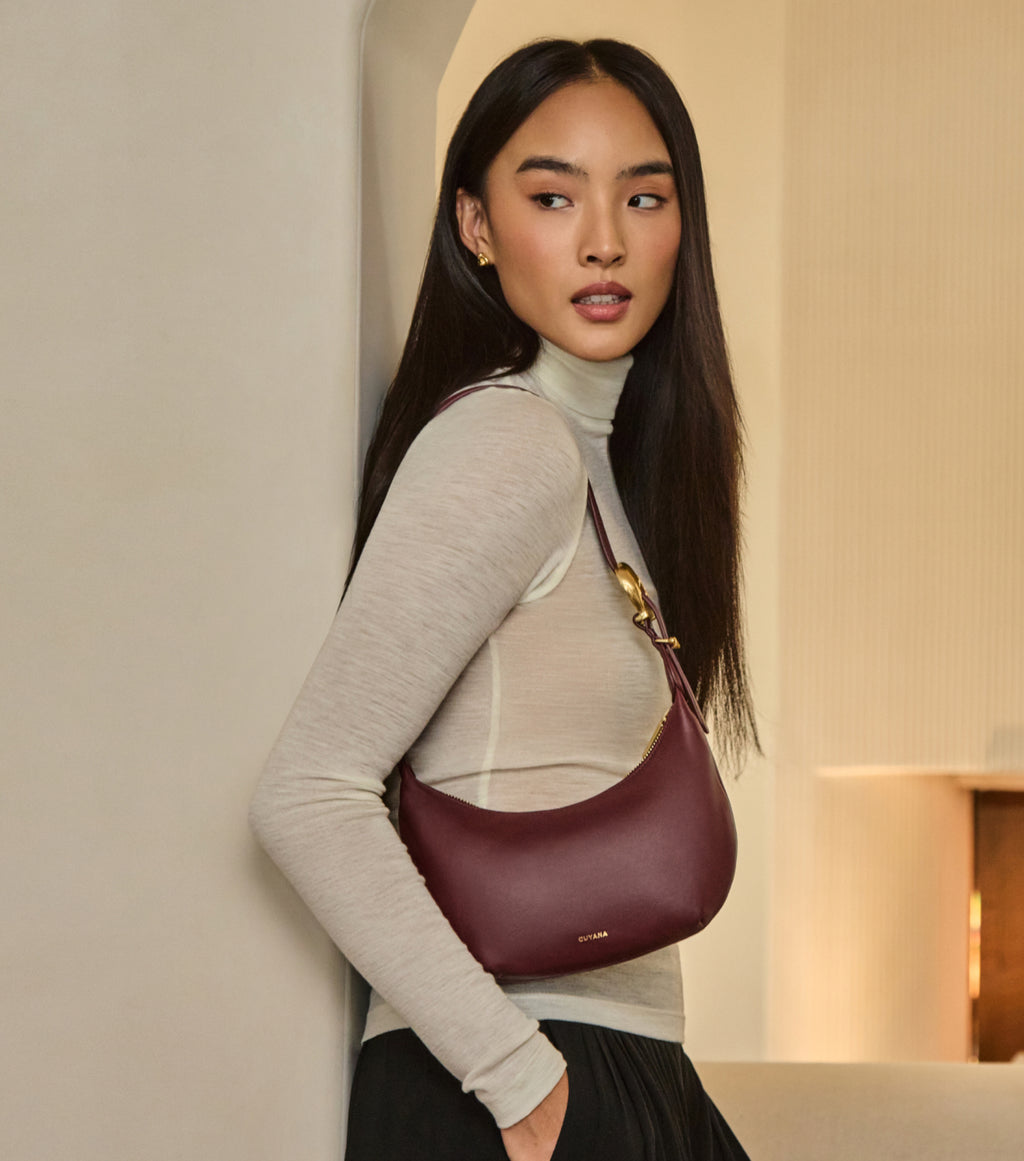 Person with shoulder bag leaning against a wall.
