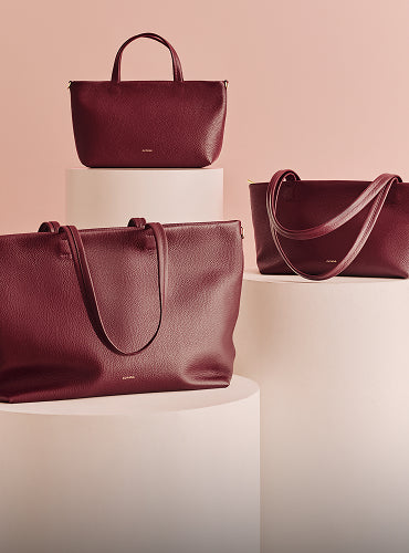 Three leather handbags displayed on white pedestals.