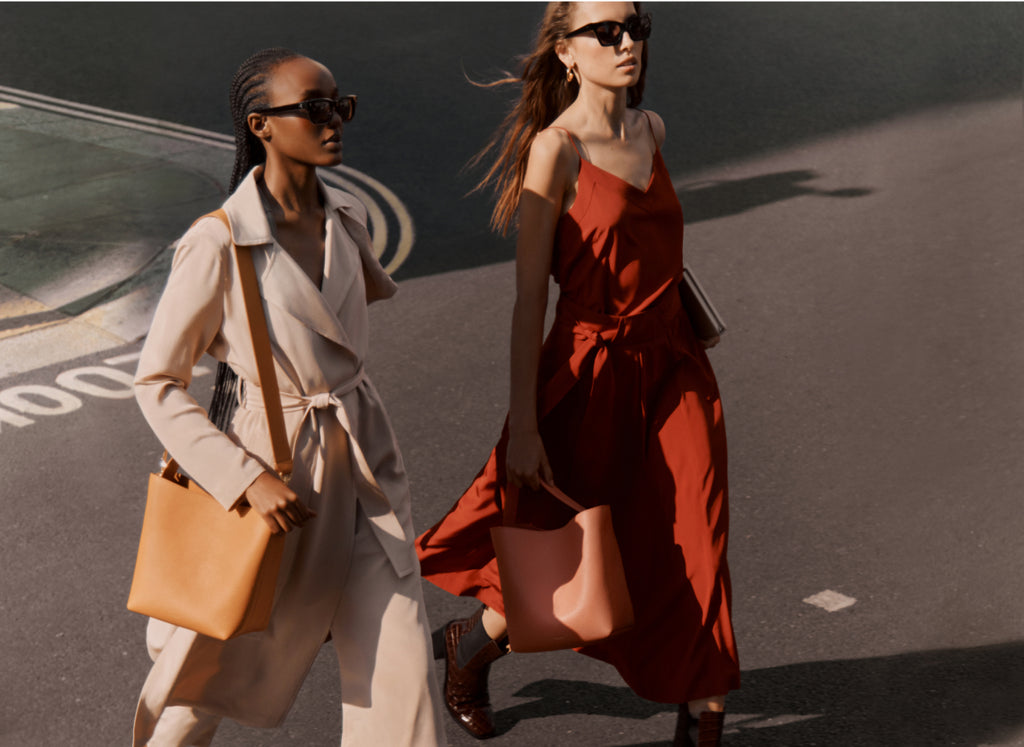 Two women walking on a street, both carrying bags.