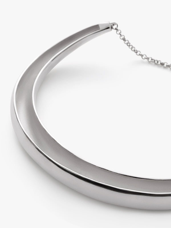 Circular metal necklace with a chain on a plain background.