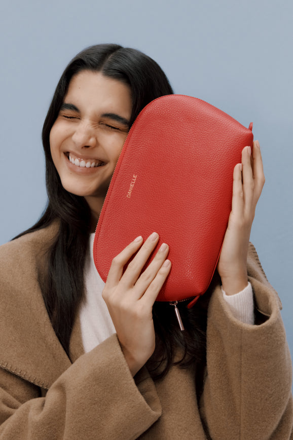 Woman holding a large pouch next to her face, smiling with closed eyes.