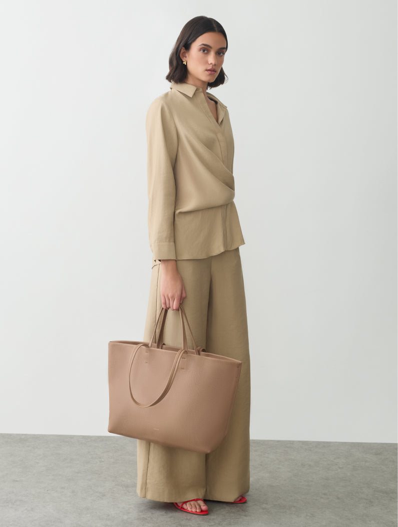 Person in matching outfit holding a large handbag, standing against a plain background.