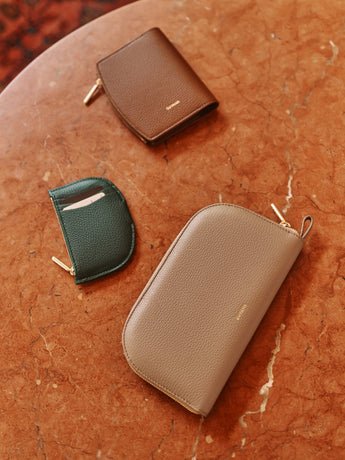 Three leather wallets with zippers on a marble table.