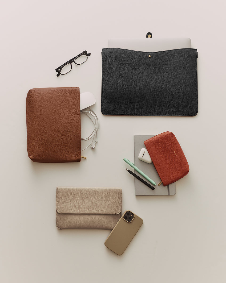 Office accessories including pouches, glasses, pens, a phone, and a laptop on a surface.