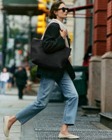 Person in a blazer and jeans carrying a large tote bag on a city street.