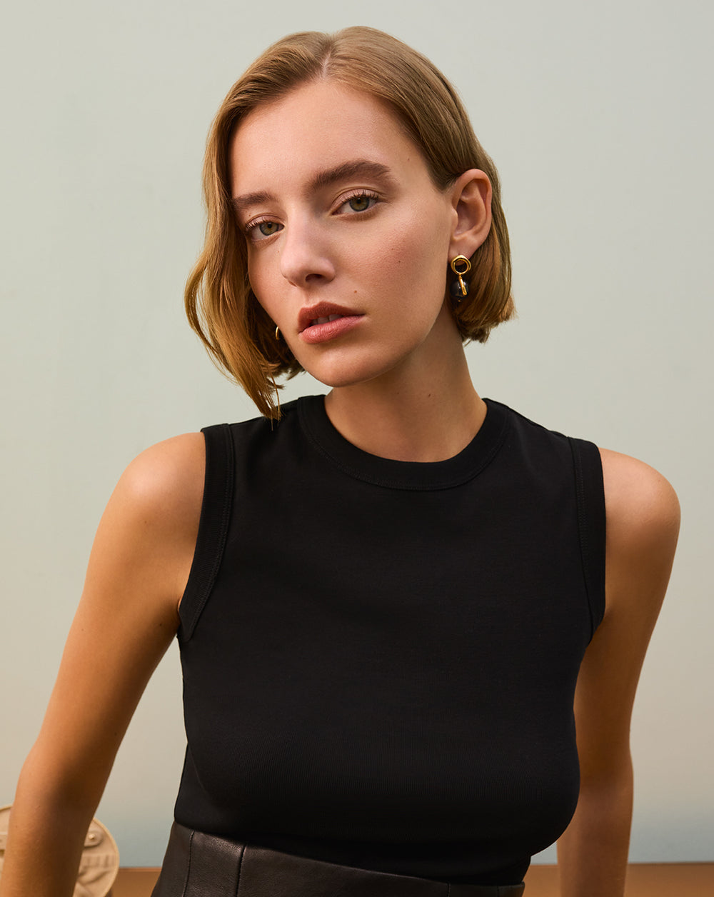 Person wearing a sleeveless top with earrings stands indoors.