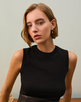 Person wearing a sleeveless top with earrings stands indoors.
