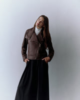 Person wearing a jacket and a long skirt, standing against a plain background.