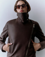 Person wearing a jacket with a high collar and sunglasses, hands in pockets.