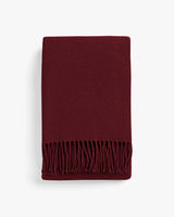 Folded fringed scarf on a plain background.