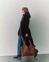 Person in a cape and jeans carrying a large bag, walking indoors.