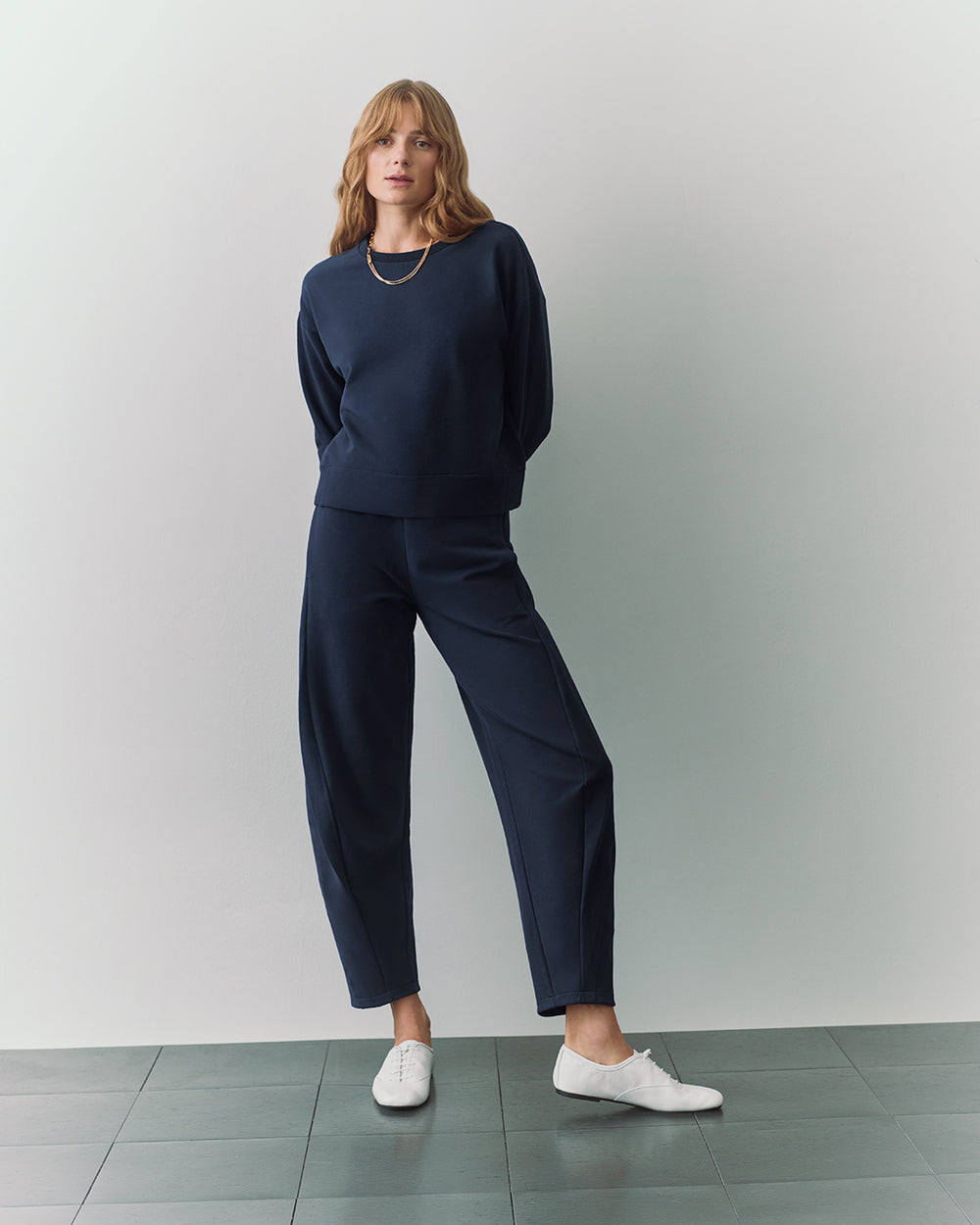 Person wearing a sweater, pants, and sneakers, standing on tiled floor.