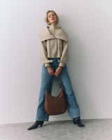 Person in cape and jeans holding a large bag, standing against a plain background.