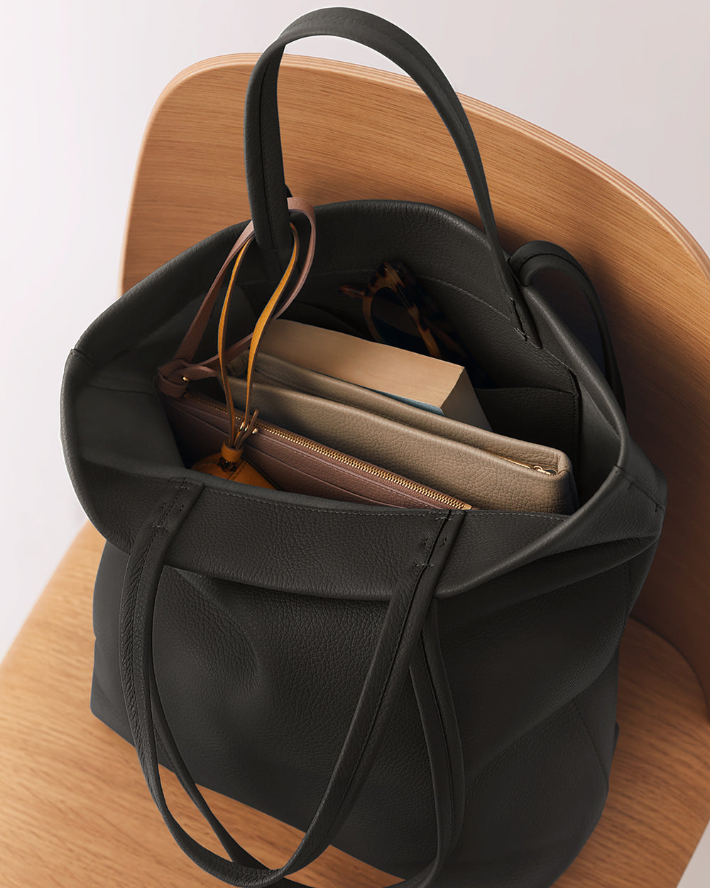 Open handbag on chair with books, glasses, and purse inside