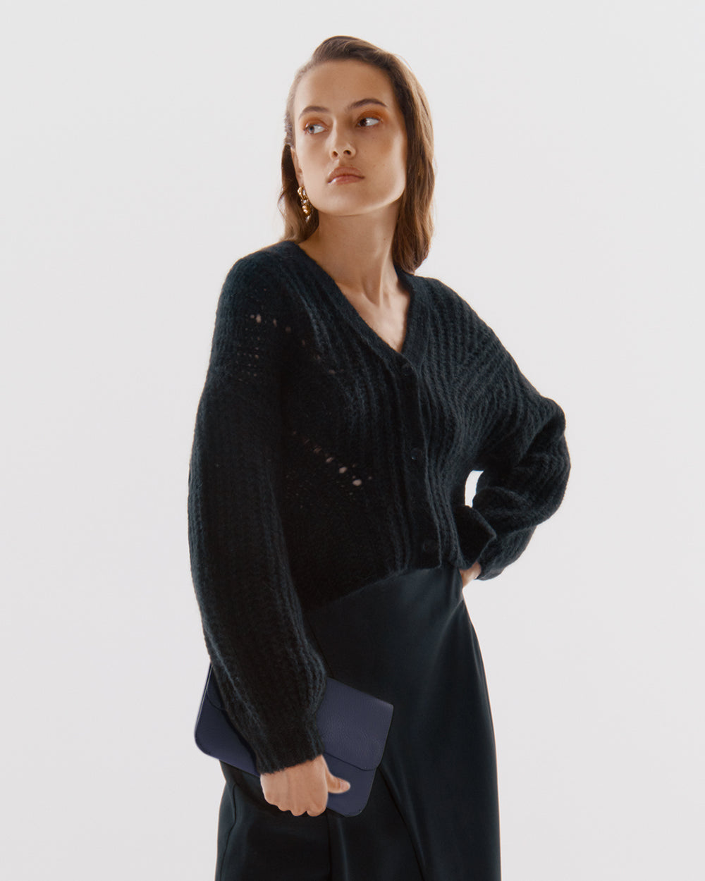 Person in a cardigan holding a small clutch.