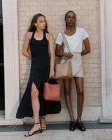 Two women posing with handbags against a brick wall.